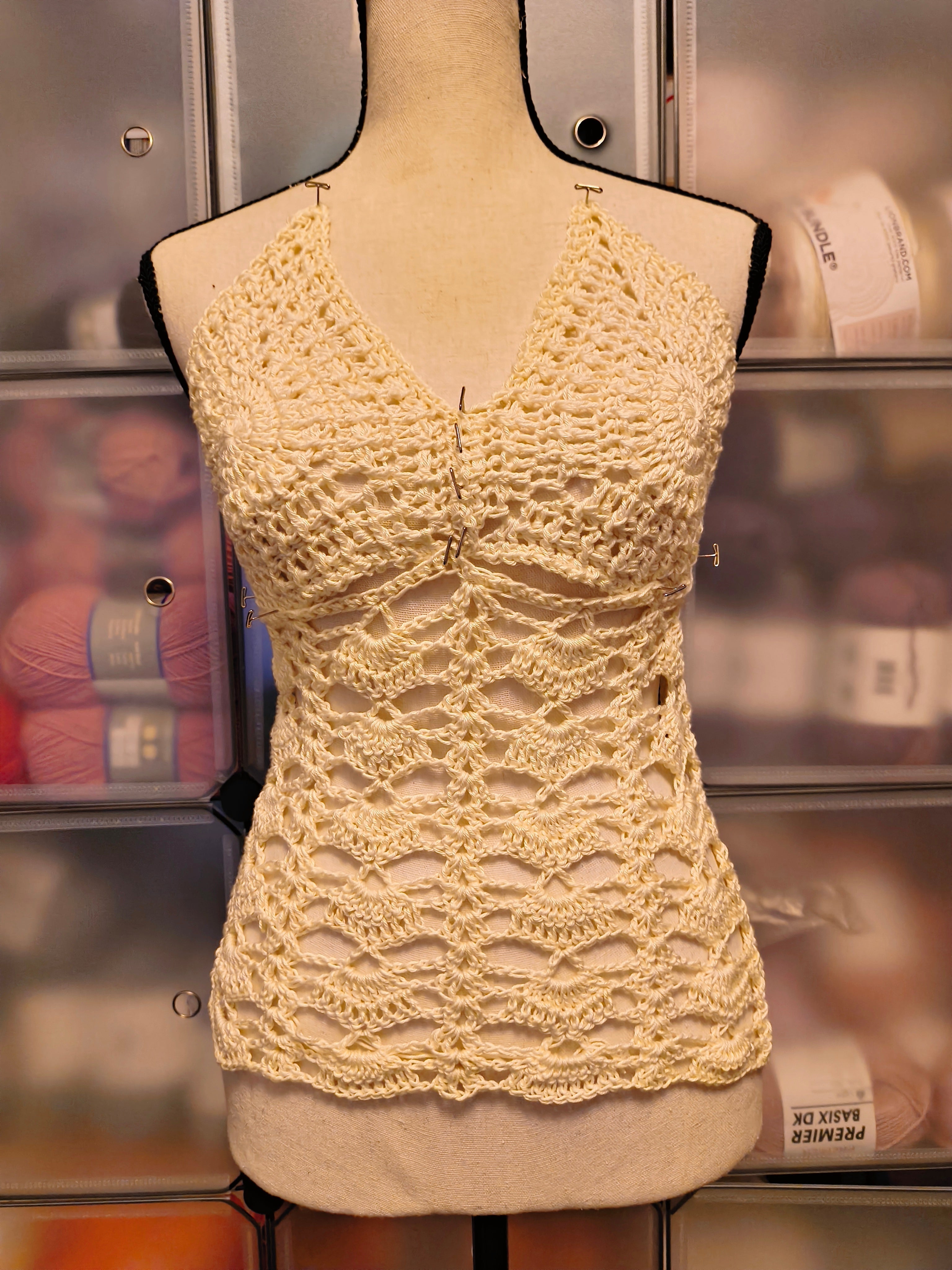 Cream-colored crochet lace top pinned on a mannequin featuring shell lace detailing and textured crochet cups in a soft boho style.