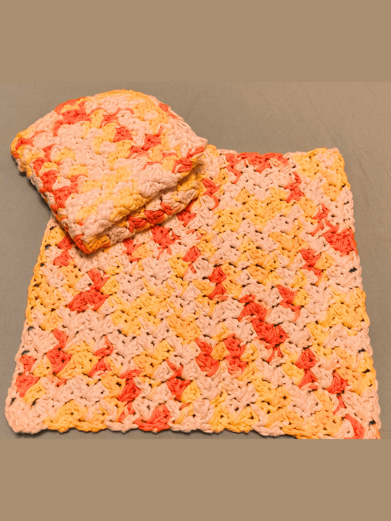 Stack of handmade crochet dishcloths in white, yellow, and orange variegated yarn, with one folded on top against a gray background.