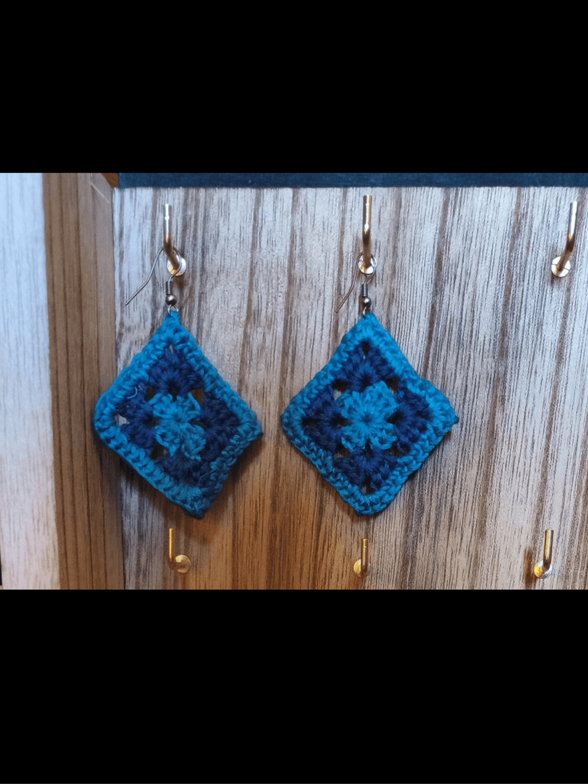 Pair of handmade granny square earrings in turquoise and dark blue, hanging as diamonds from silver-tone fishhook wires.