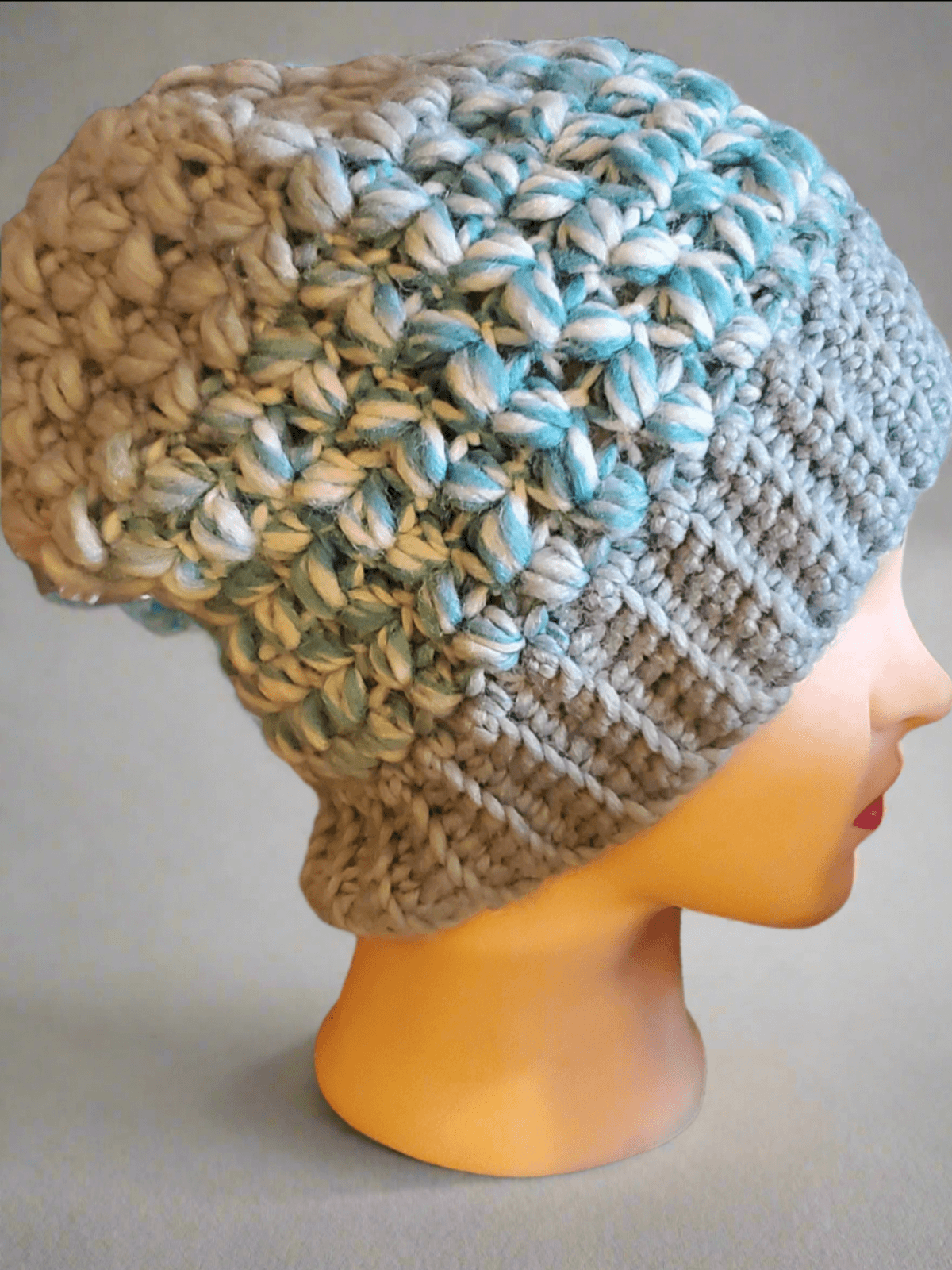 Side view of a chunky light blue and cream crochet slouchy beanie with textured stitches, displayed on a mannequin head.