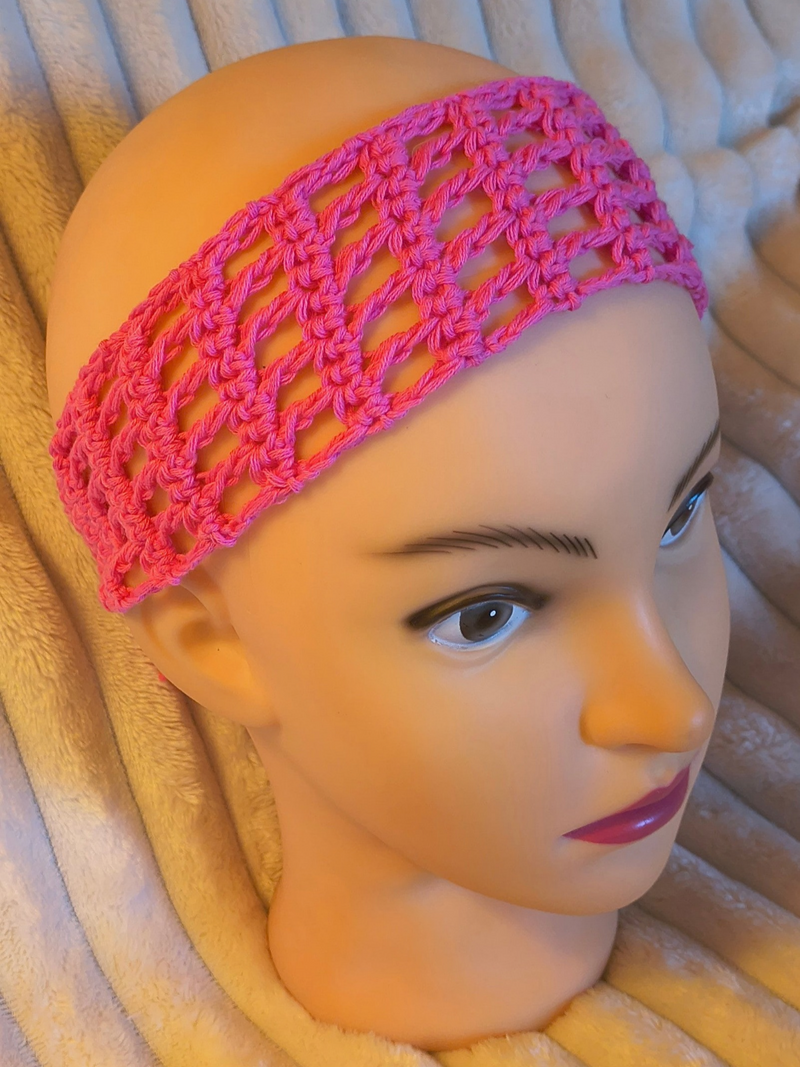 Bright pink openwork crochet headband worn on a mannequin head, showing its wide lace pattern across the forehead.