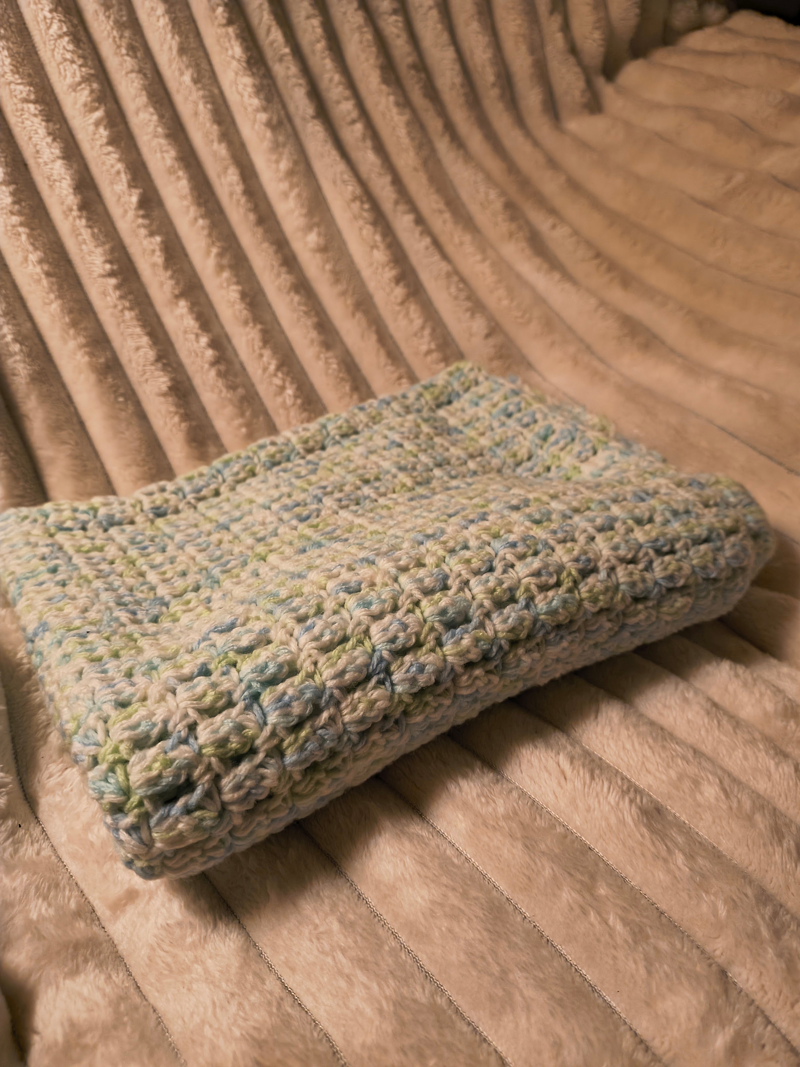 Crochet blue green and white baby blanket on cream blanket background
