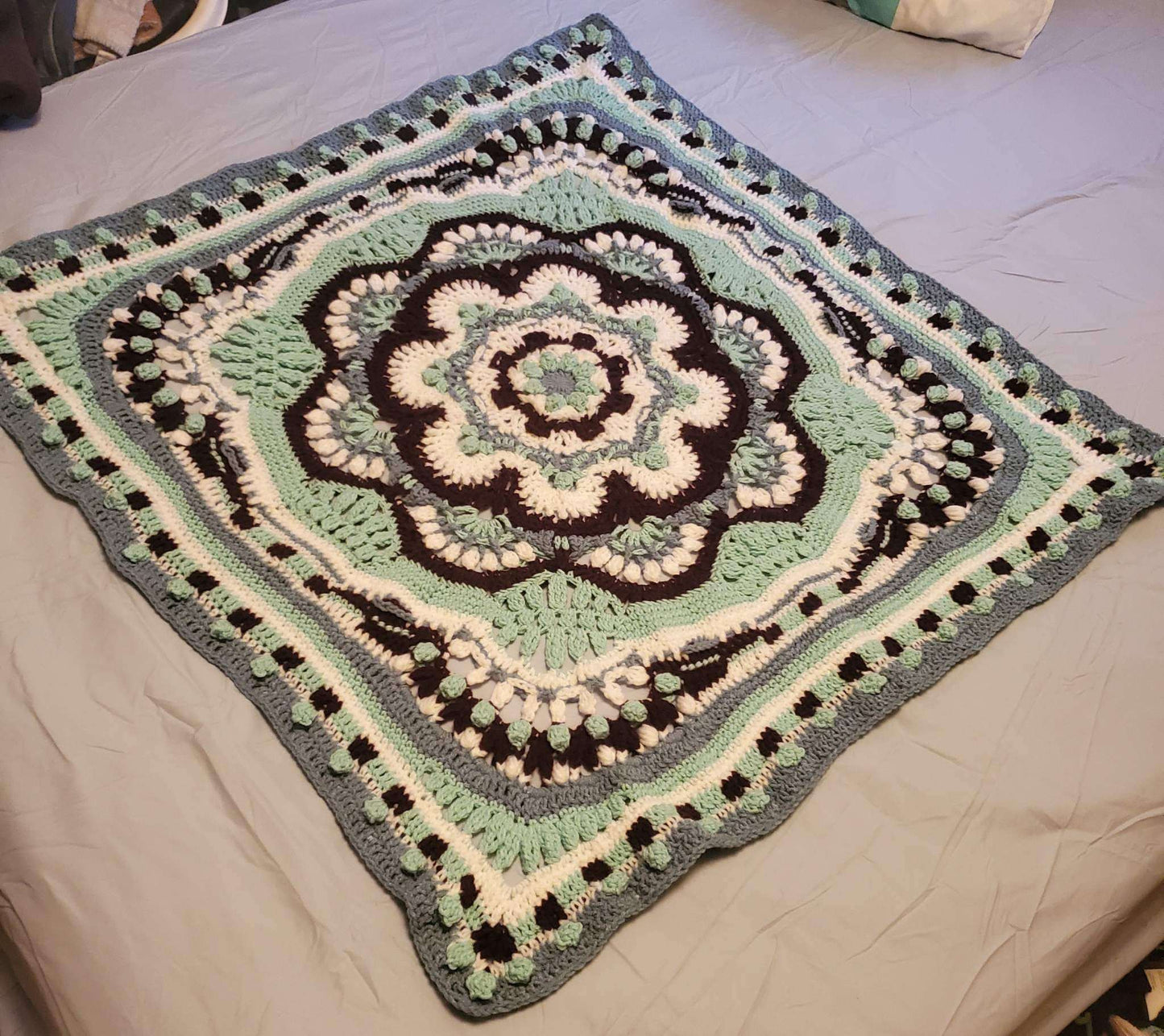 Crocheted Heritage mandala baby girl blanket, 42 inches square, with intricate design on a bed.
