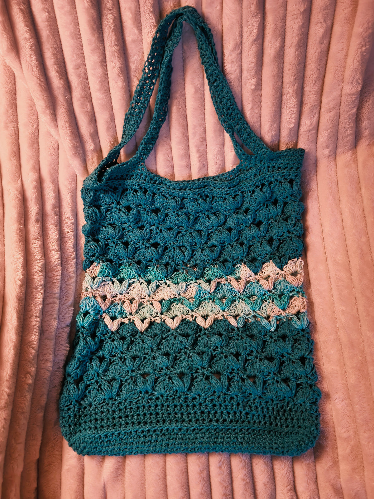 Oversized handmade crochet market bag in turquoise blue and Evening Sea variegated cotton, featuring shades of dark blue, aqua, and cream, displayed flat to show the full design and long shoulder straps.