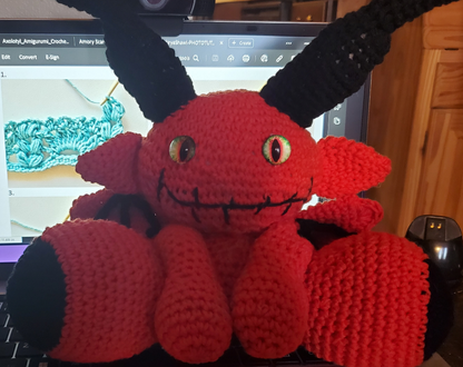 Lil Red Devil crocheted handmade toy with black horns, displayed on a laptop.
