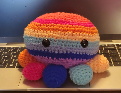 Handmade crocheted rainbow octopus toy with hidden compartment, placed on a laptop.