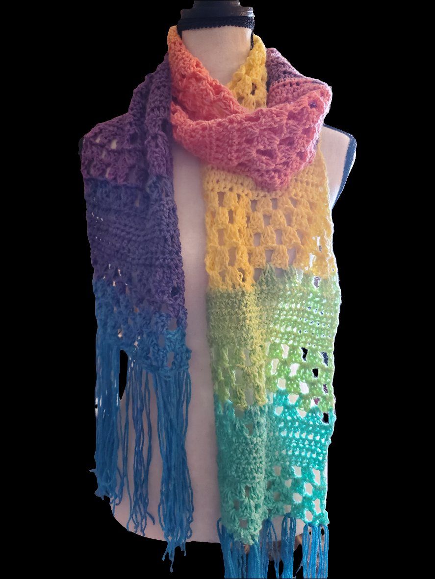 Handmade crochet scarf in bright rainbow gradient colors with a lightweight open stitch pattern and fringe ends, draped on a dress form against a dark background.