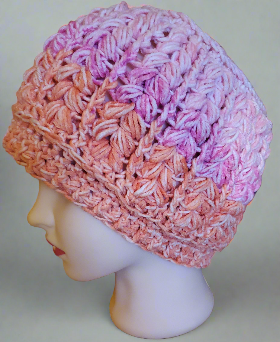 Handmade crochet beanie in orange and pink ombre yarn, featuring a thick textured feather stitch design on a mannequin head.