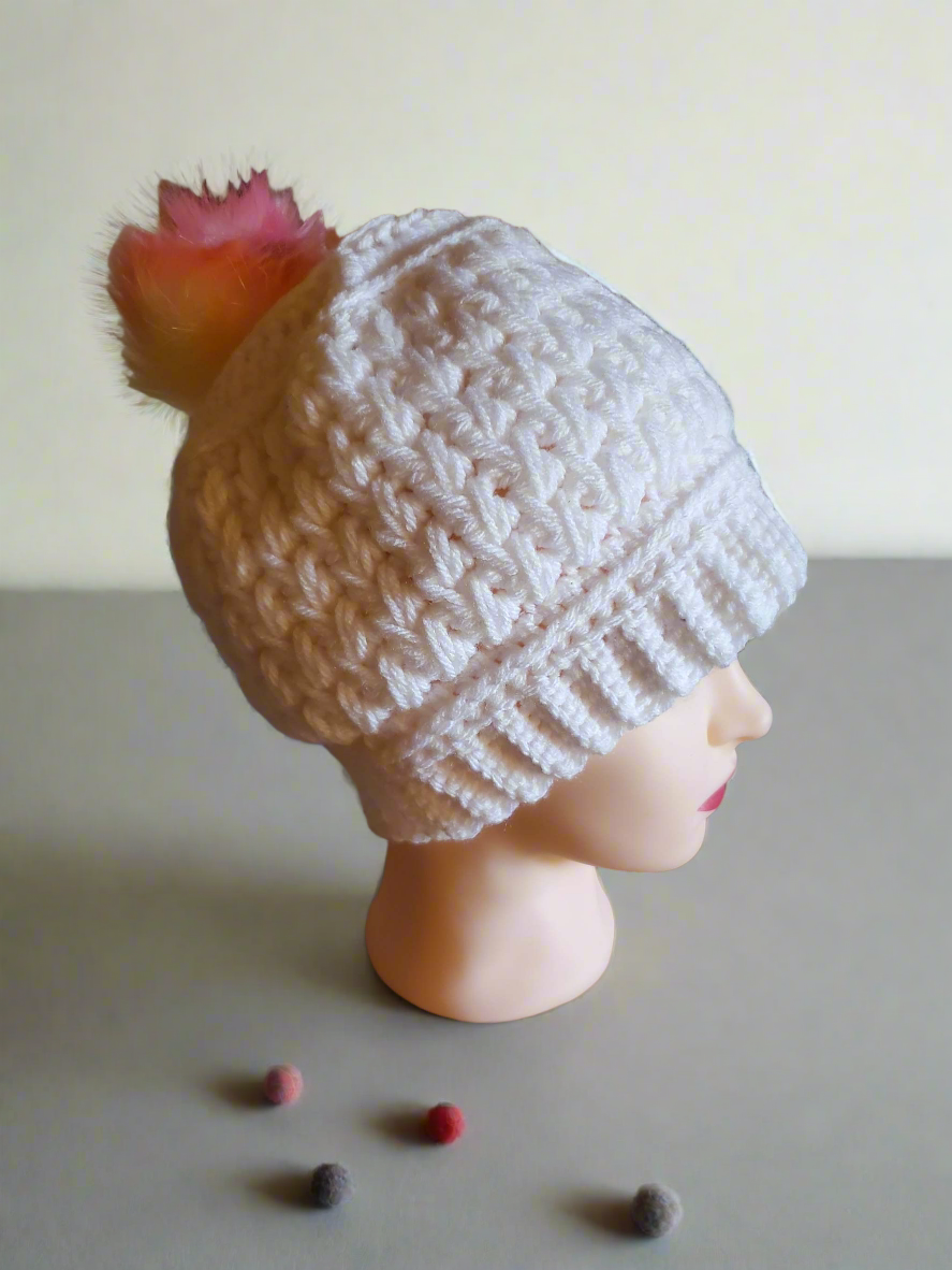 white crochet beanie with feather stitch texture and rainbow pom pom on mannequin head