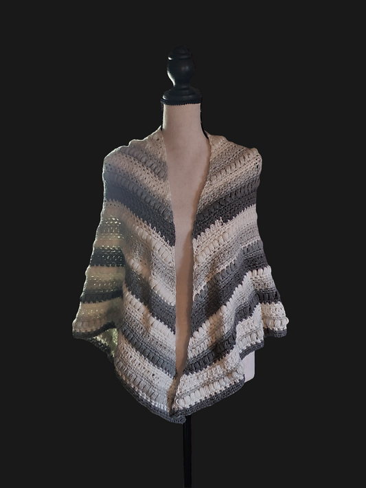Handmade crochet shawl in neutral gray and cream stripes with rich textured stitches, large and draping elegantly over a dress form against a dark background.