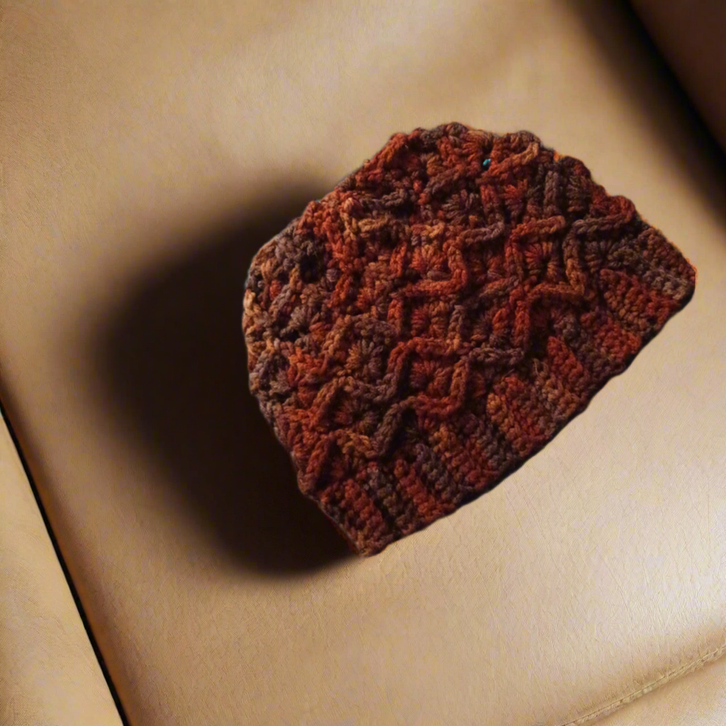 Handmade variegated dark brown crocheted winter beanie hat on a beige surface.