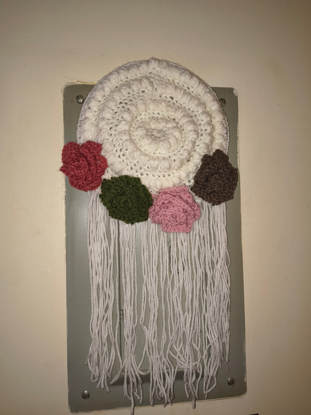 Handmade fiber art wall hanging with crochet flowers and fringe in soft, warm lighting showing detailed texture and boho style design