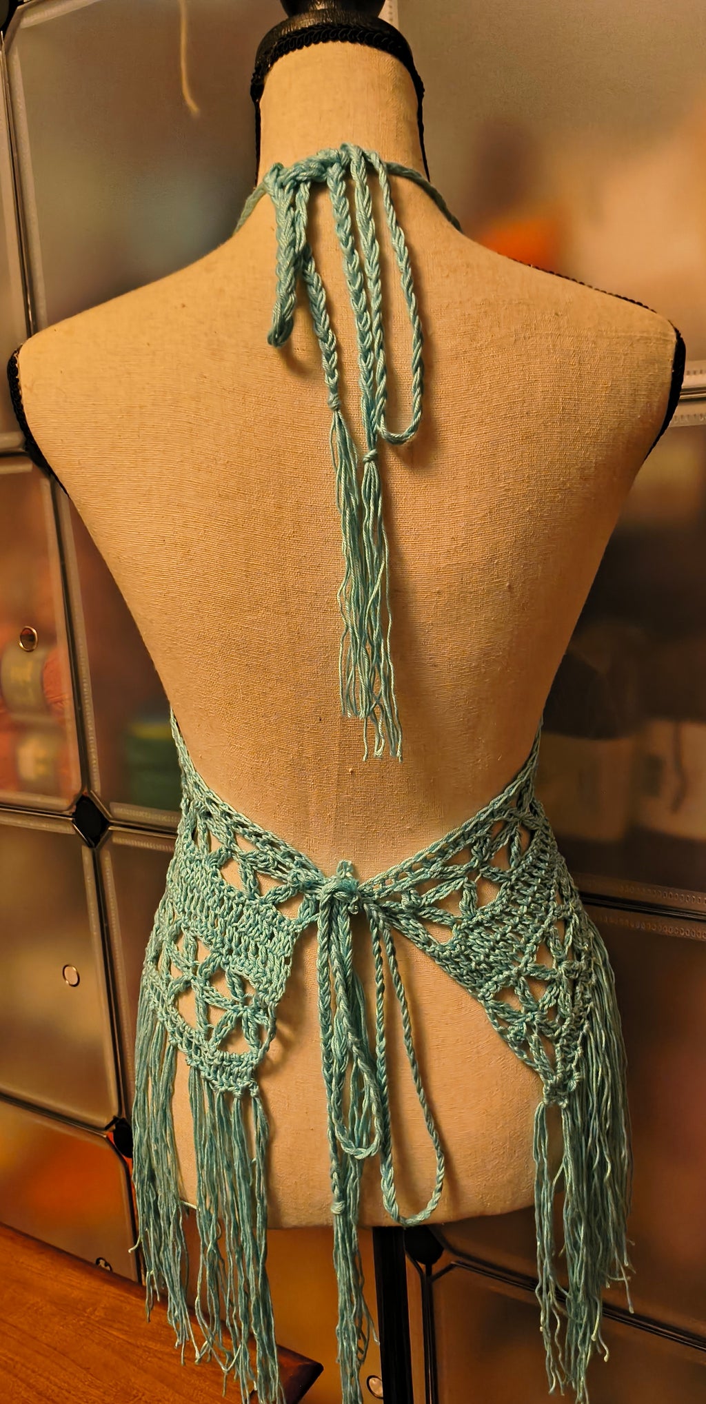 Back view of light blue crochet halter top with braided neck ties and adjustable back ties, featuring open lace sides and fringe detail