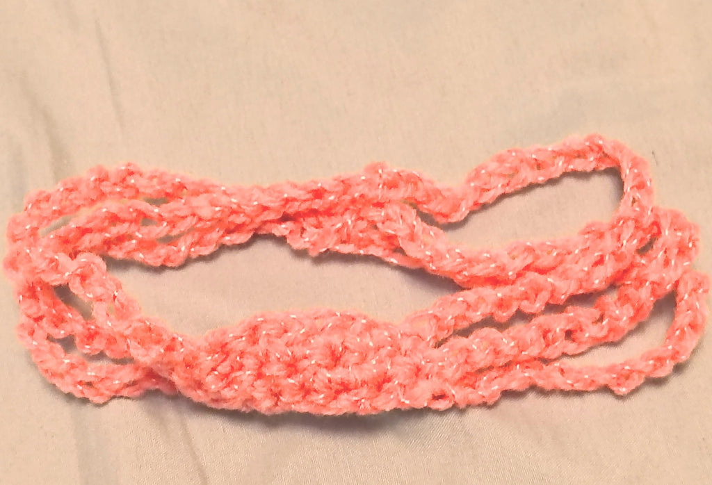 Soft pink crochet baby headband with simple textured center and stretchy band, handmade newborn headband laid flat on a neutral background