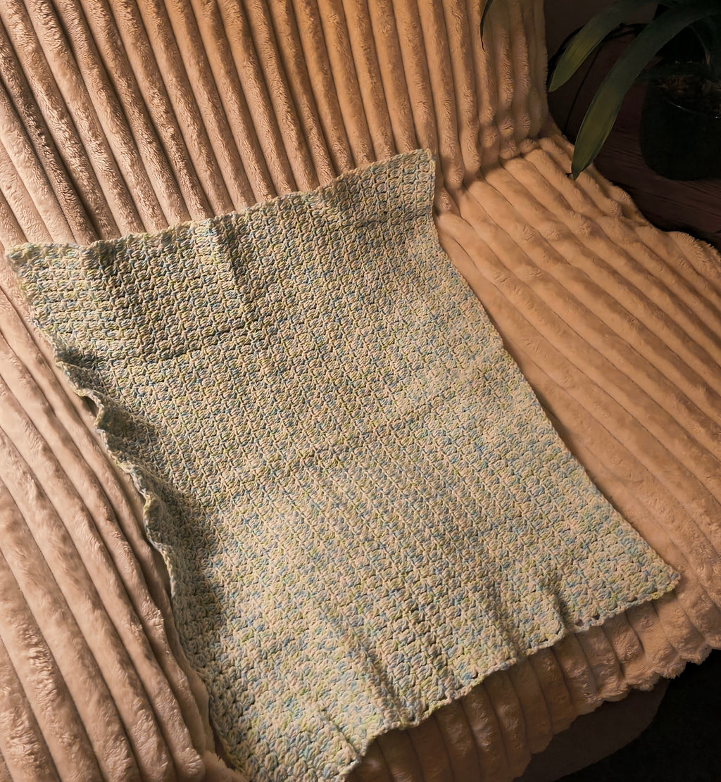 Handmade crochet baby blanket in soft blue, green, and white tones, lightweight stroller size with textured stitch detail, measuring approximately 29 by 22 inches