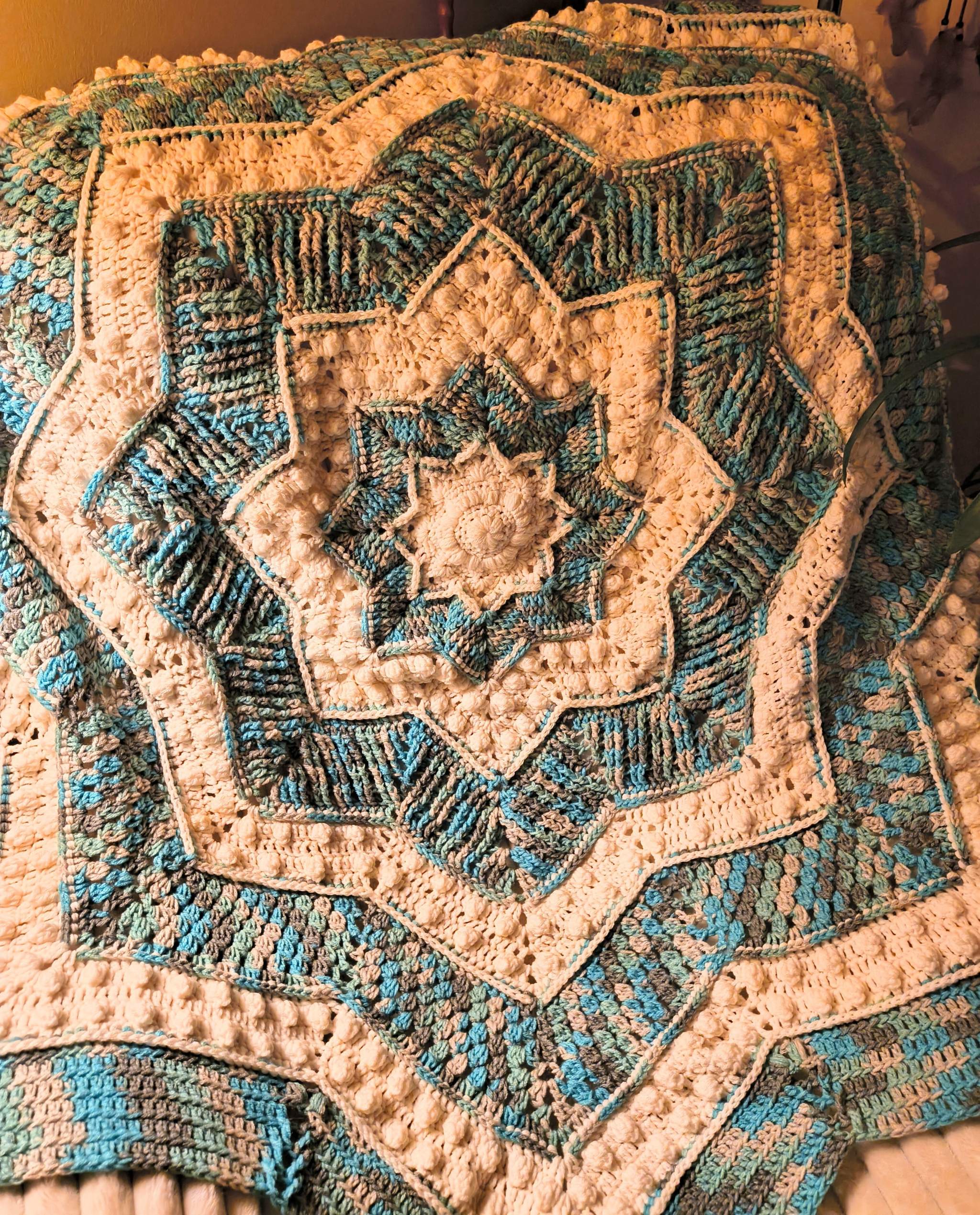 Large handmade crochet star blanket draped over a chair, featuring a bold mandala pattern in blue, gray, and white tones