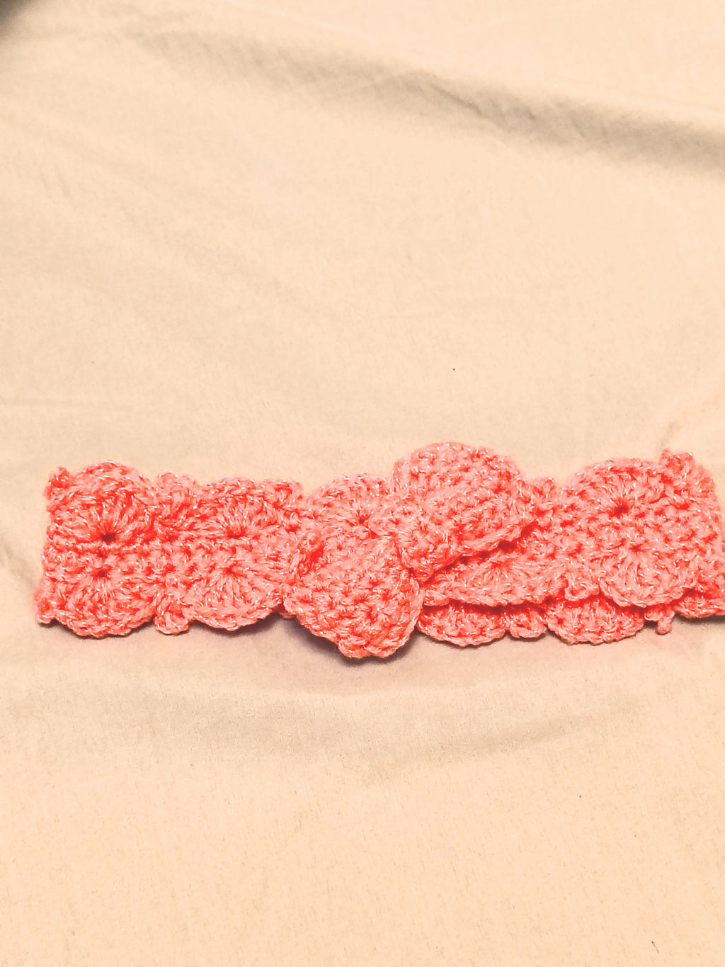 Soft pink crochet baby headband with bow detail, handmade newborn headband laid flat on a neutral background