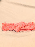 Soft pink crochet baby headband with bow detail, handmade newborn headband laid flat on a neutral background