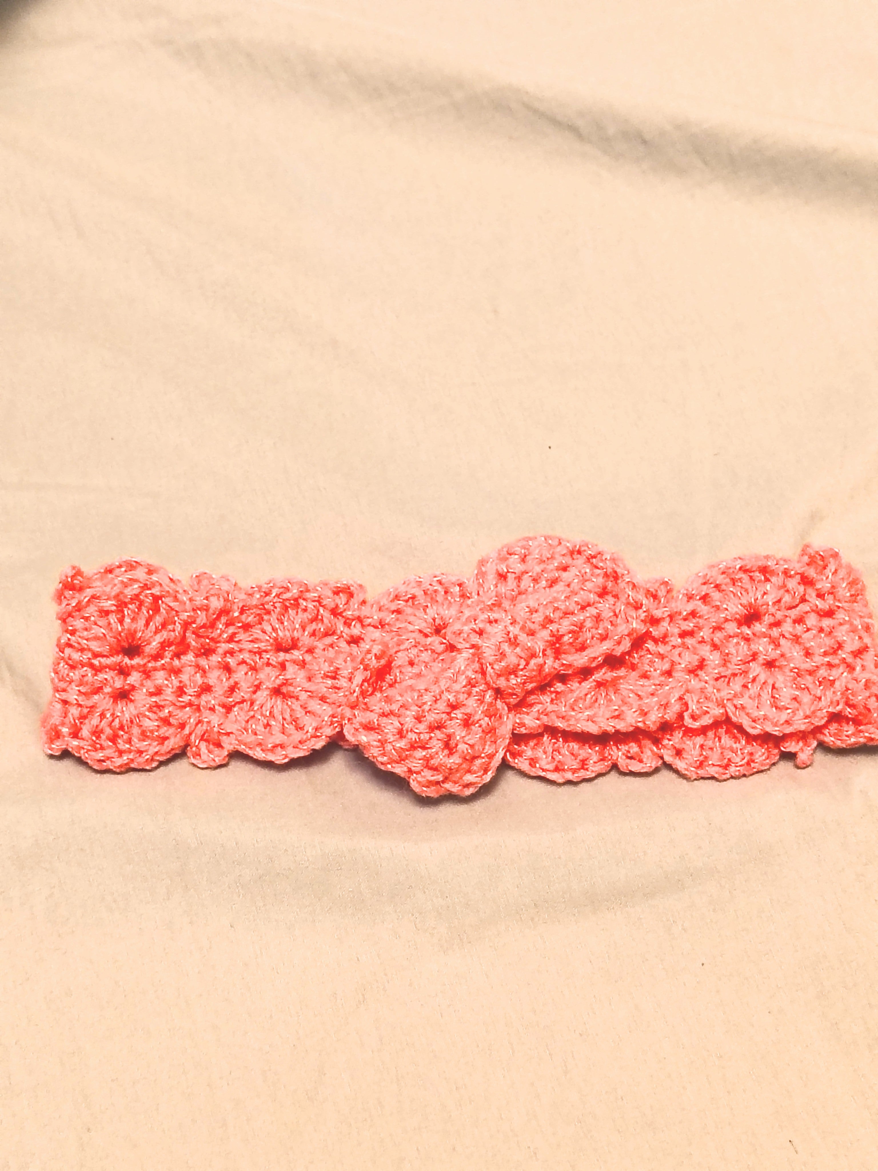 Soft pink crochet baby headband with bow detail, handmade newborn headband laid flat on a neutral background