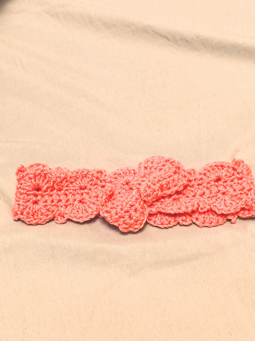 Soft pink crochet baby headband with bow detail, handmade newborn headband laid flat on a neutral background