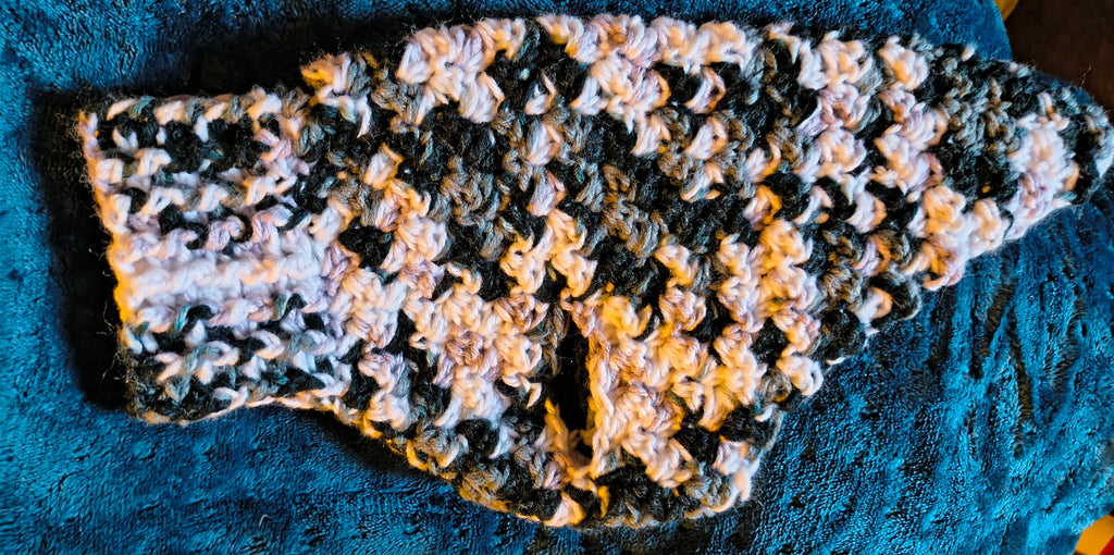 Handmade black, gray and white crochet dog sweater for extra-small to small dogs displayed flat on a blue blanket.