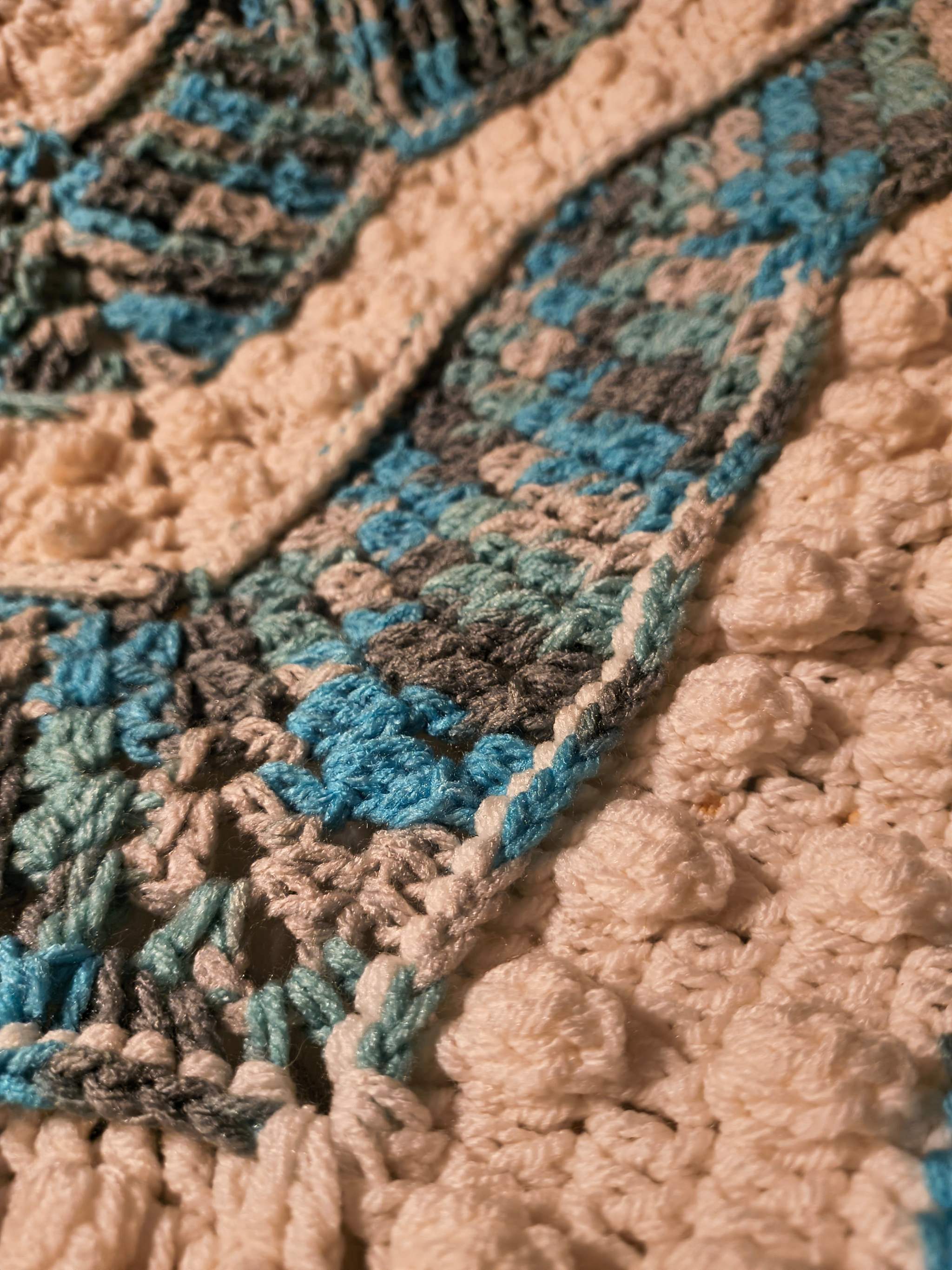 Close-up of crochet star blanket showing intricate textured stitches in blue, gray, white, and camouflage color palette
