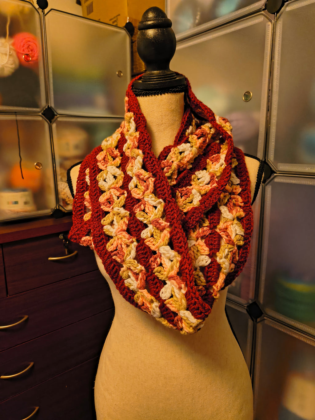 Handmade crochet infinity scarf with dimensional floral stitch details in burgundy, blush peach, cream, olive green, and brown tones displayed on a dress form.