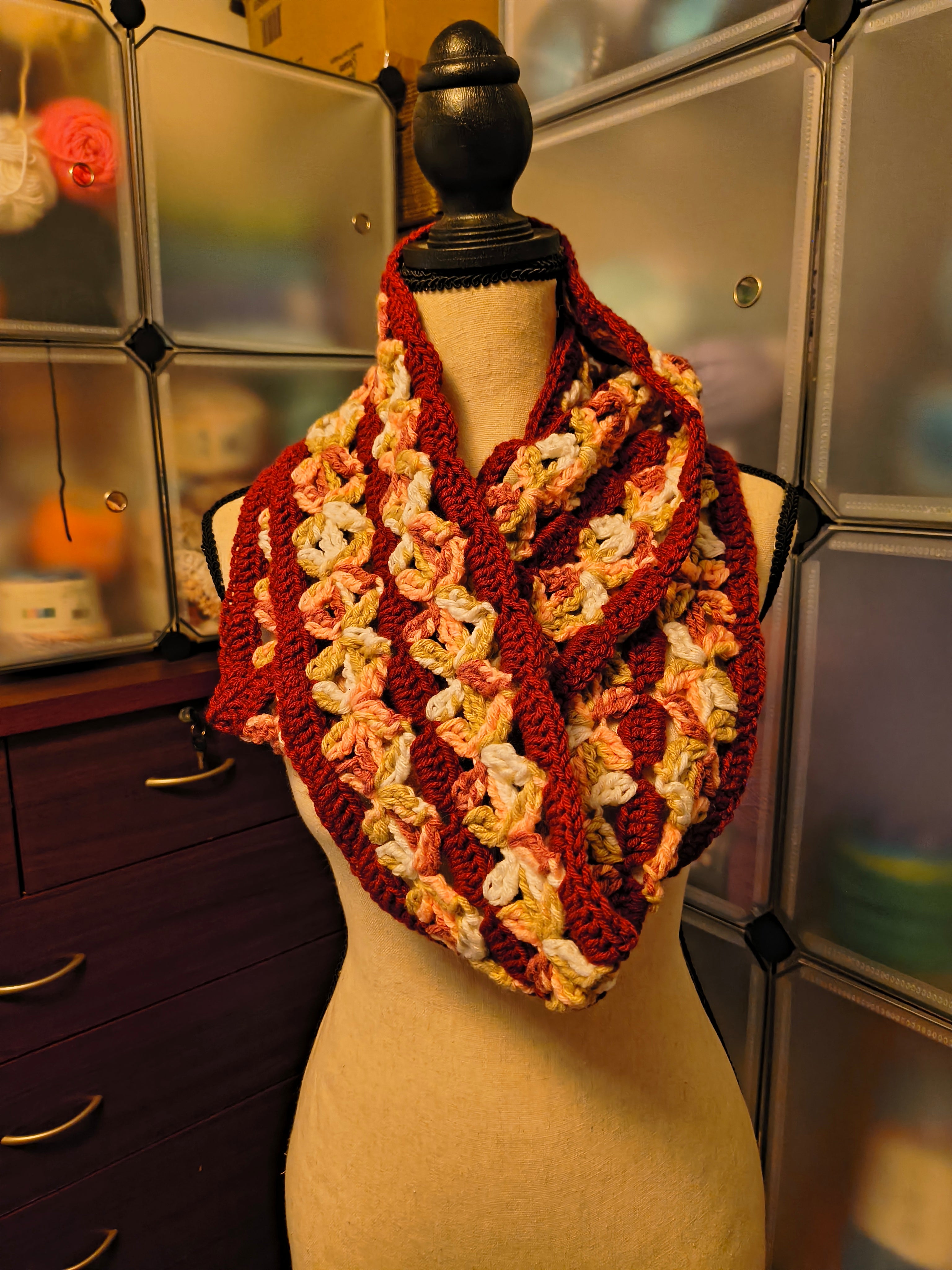 Handmade crochet infinity scarf with dimensional floral stitch details in burgundy, blush peach, cream, olive green, and brown tones displayed on a dress form.
