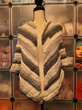 Handmade crochet triangle shawl wrap featuring textured puff stitch detailing in soft cream, silver gray, and charcoal tones with an elegant drape.