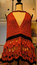 Warm-toned mannequin displaying a handmade crochet halter top in rust orange and black acrylic yarn, featuring textured cups, an open lace lower panel with scalloped edging, and a corset-style lace-up back for an adjustable fit