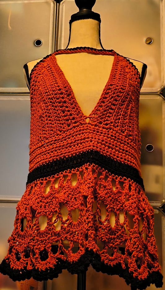 Handmade crochet halter top in rust and black, featuring a deep V neckline, fitted bodice, and intricate lace hem with openwork detailing, displayed on a dress form.