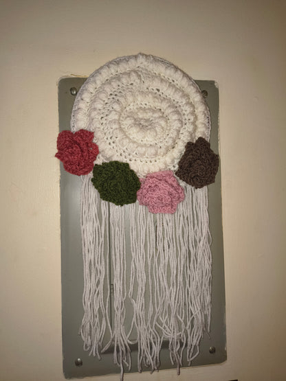 Handmade fiber art wall hanging with crochet flowers and fringe in soft, warm lighting showing detailed texture and boho style design