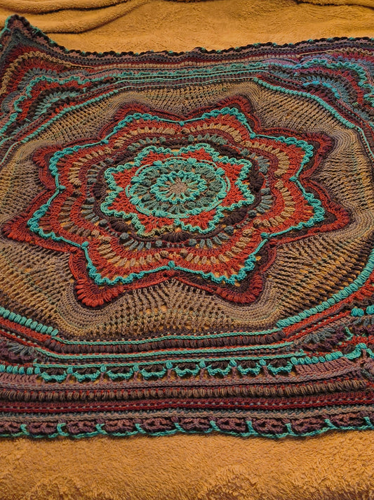 Large handmade crochet mandala blanket in teal, purple, light gray, and dark gray displayed flat on a queen-size bed, featuring intricate layered textures and a bold geometric floral design