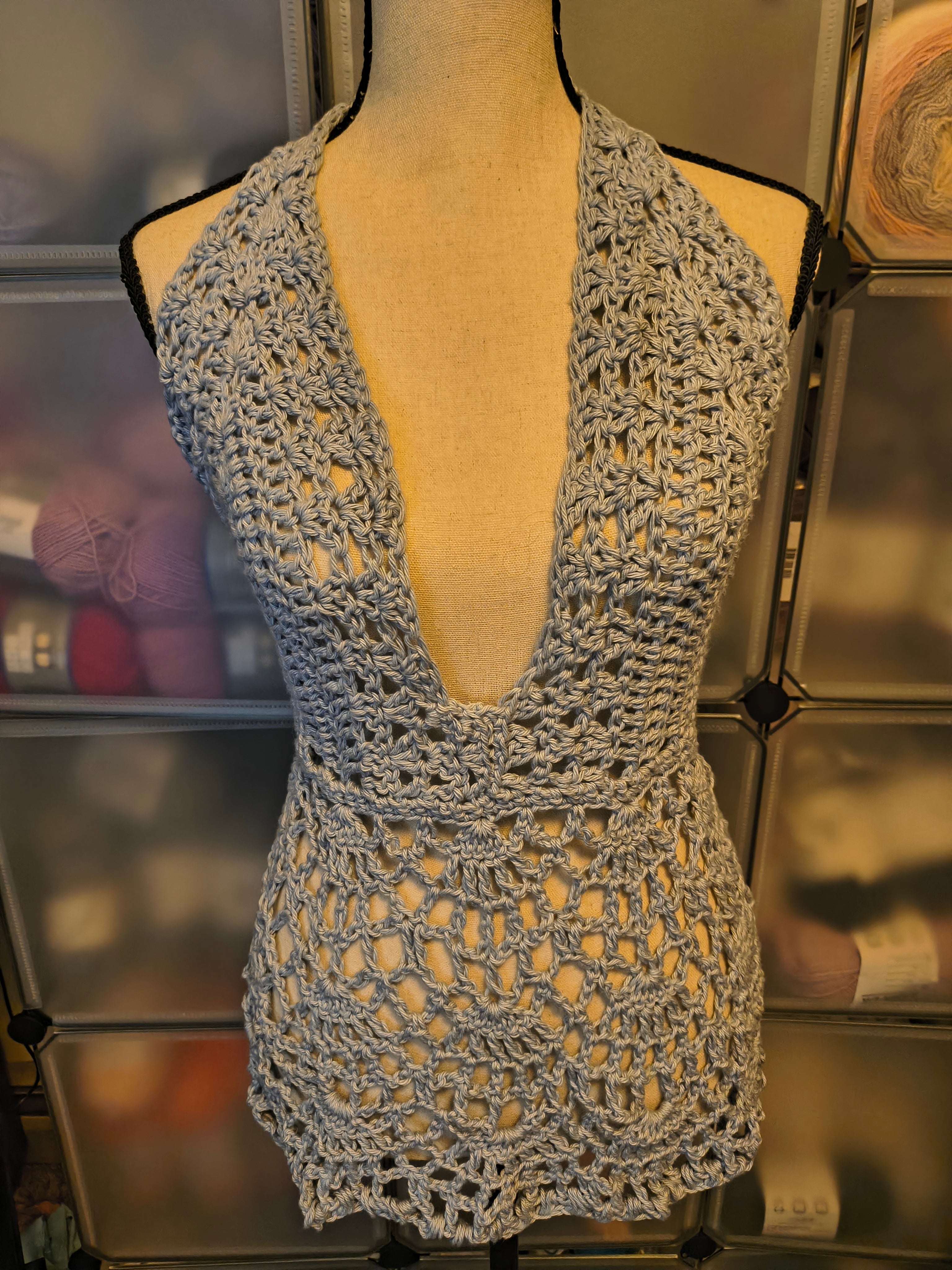 Handmade light silvery blue crochet halter top displayed on a dress form, featuring a deep V-neckline, intricate lace skirt, and adjustable open-back design.