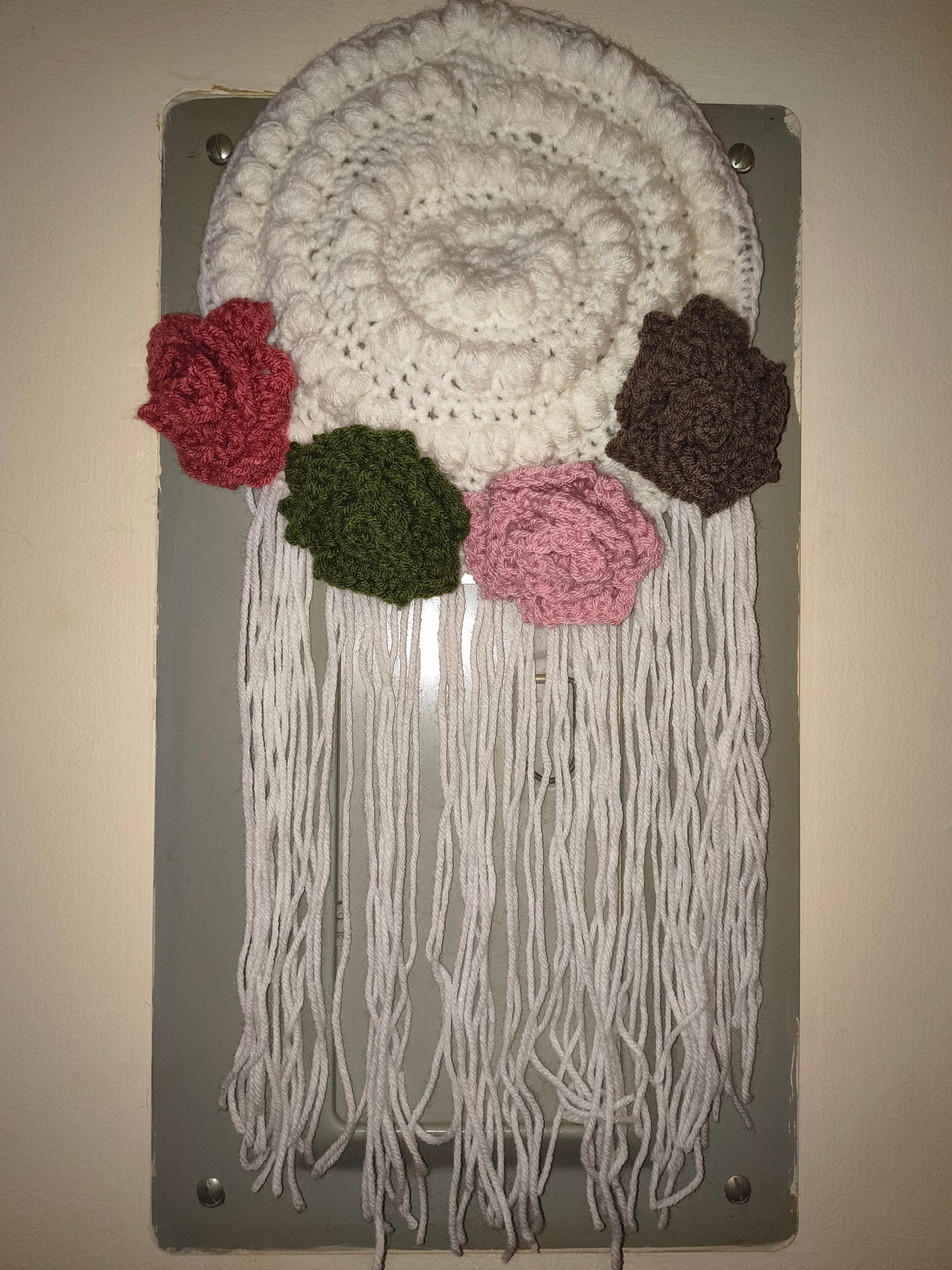 Boho crochet wall hanging with textured stitches, floral accents, and long fringe hanging on a wall in natural lighting