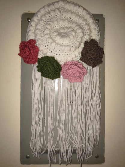 Boho crochet wall hanging with textured stitches, floral accents, and long fringe hanging on a wall in natural lighting