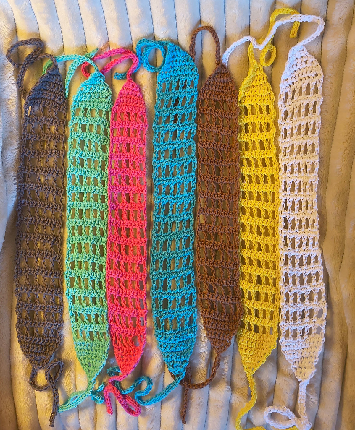 Seven handmade openwork crochet tie headbands in gray, green, pink, blue, brown, yellow and white displayed side by side.