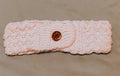 Handmade white crochet headband ear warmer with textured stitch pattern and wooden flower button closure on a neutral background