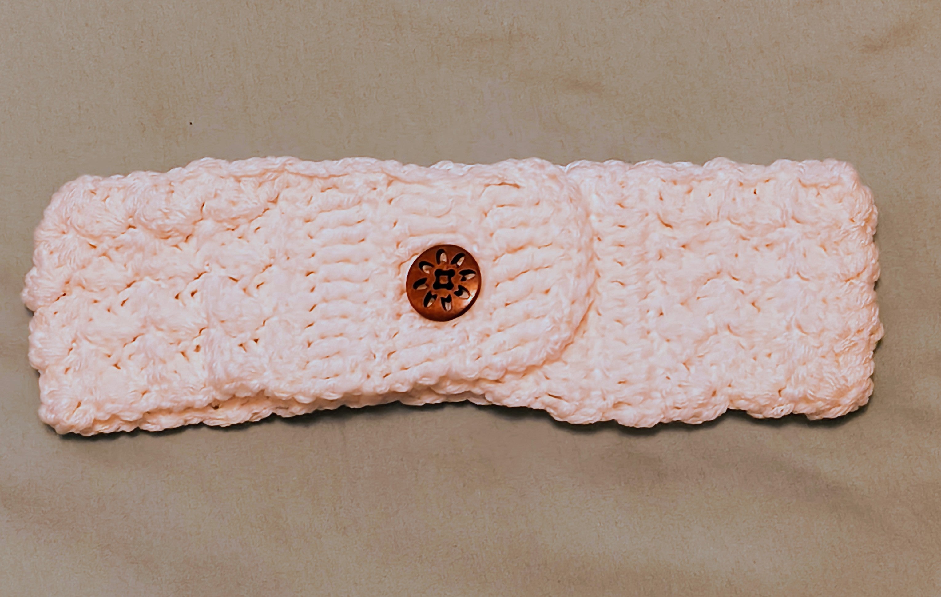 Handmade white crochet headband ear warmer with textured stitch pattern and wooden flower button closure on a neutral background
