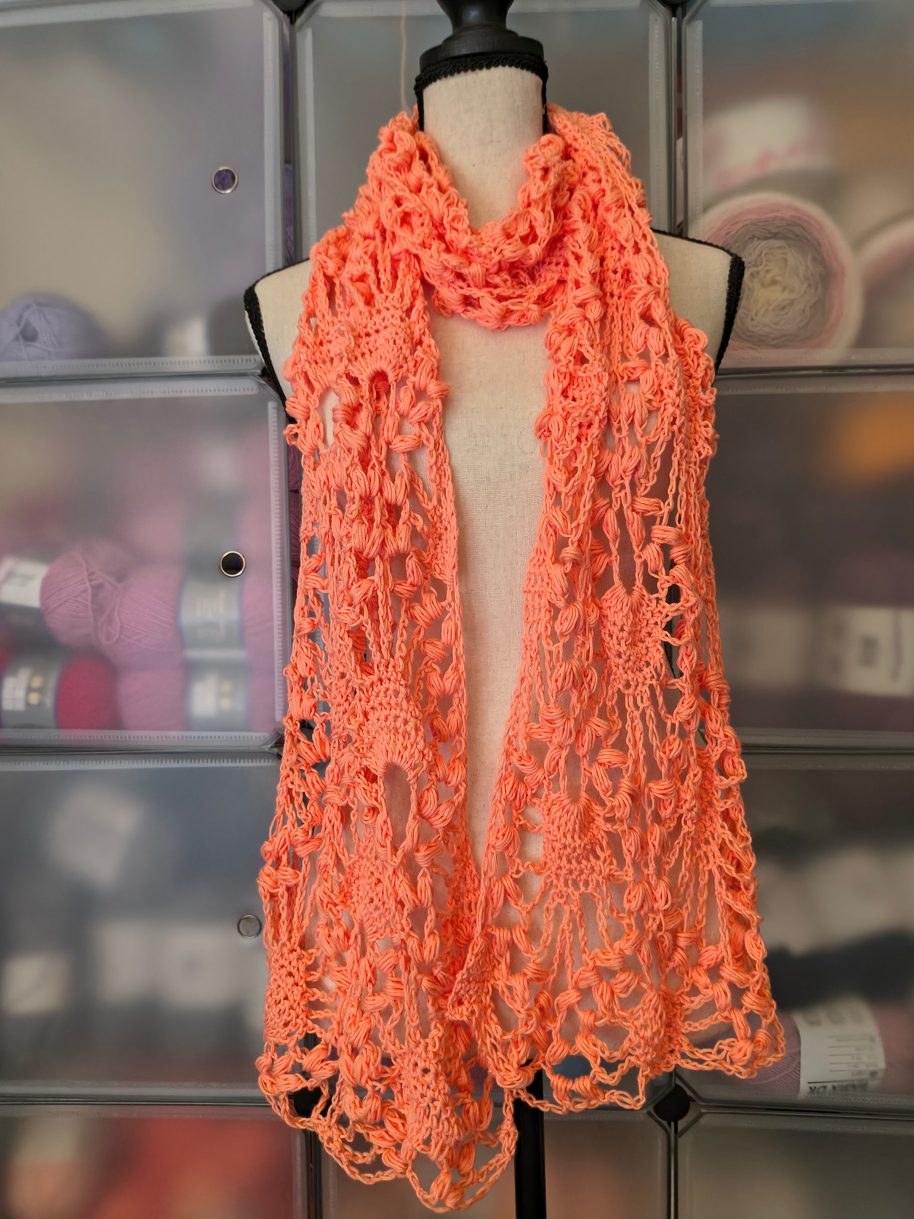 Handmade coral crochet lace scarf displayed on a dress form featuring an elegant open lace design with textured puff stitches.
