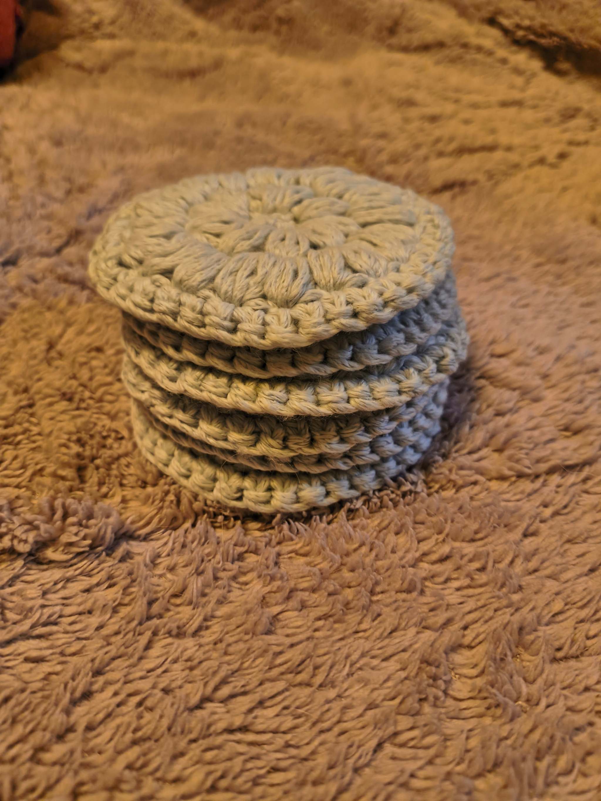 Set of six handmade crochet face scrubbies in light silver gray stacked neatly, showing soft textured cotton blend yarn and reusable skincare pads.