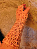 Pink crochet fingerless gloves with a shell stitch lace pattern and extended length, worn on hands and wrists, showing detailed texture and soft yarn.
