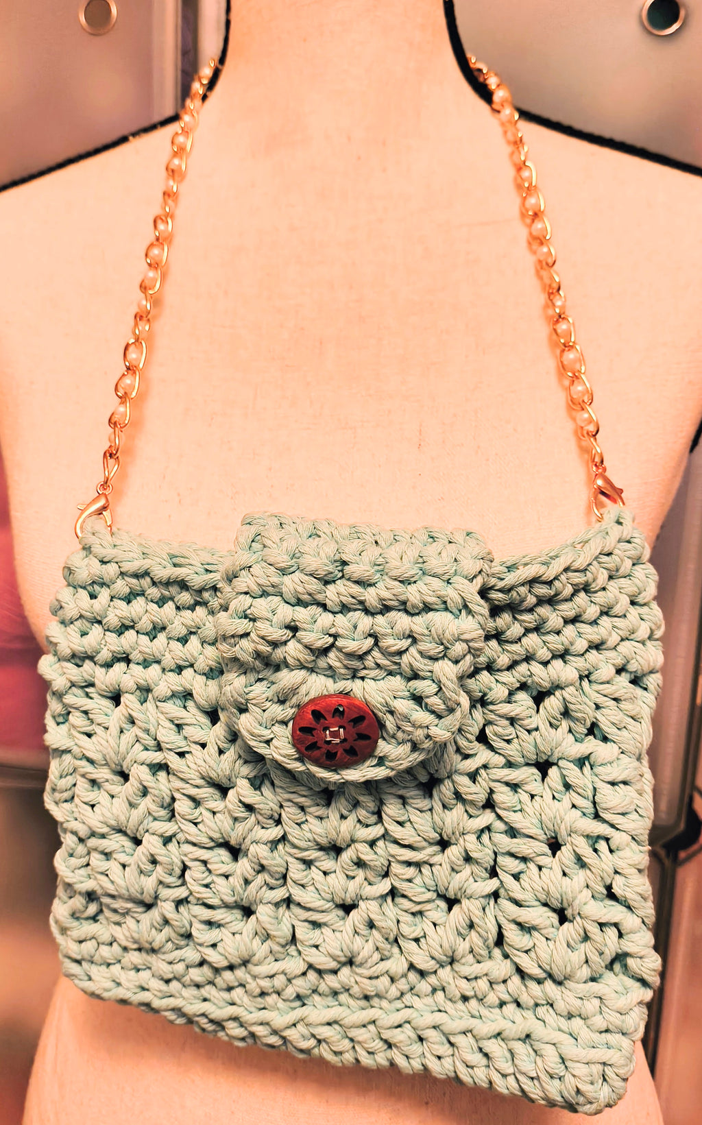 Front view of aqua crochet purse on dress form showing textured stitch pattern and button closure.