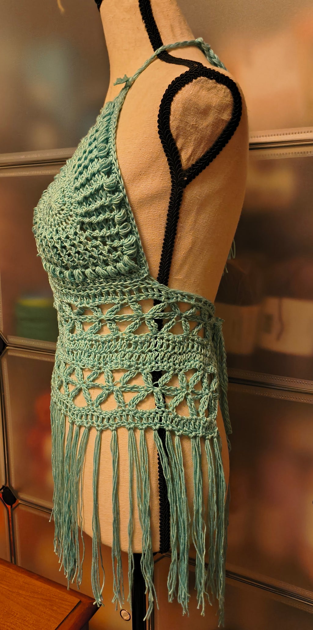 Side view of light blue crochet boho halter top on mannequin, showing textured cup shaping, open lace band design, and flowing fringe with adjustable ties