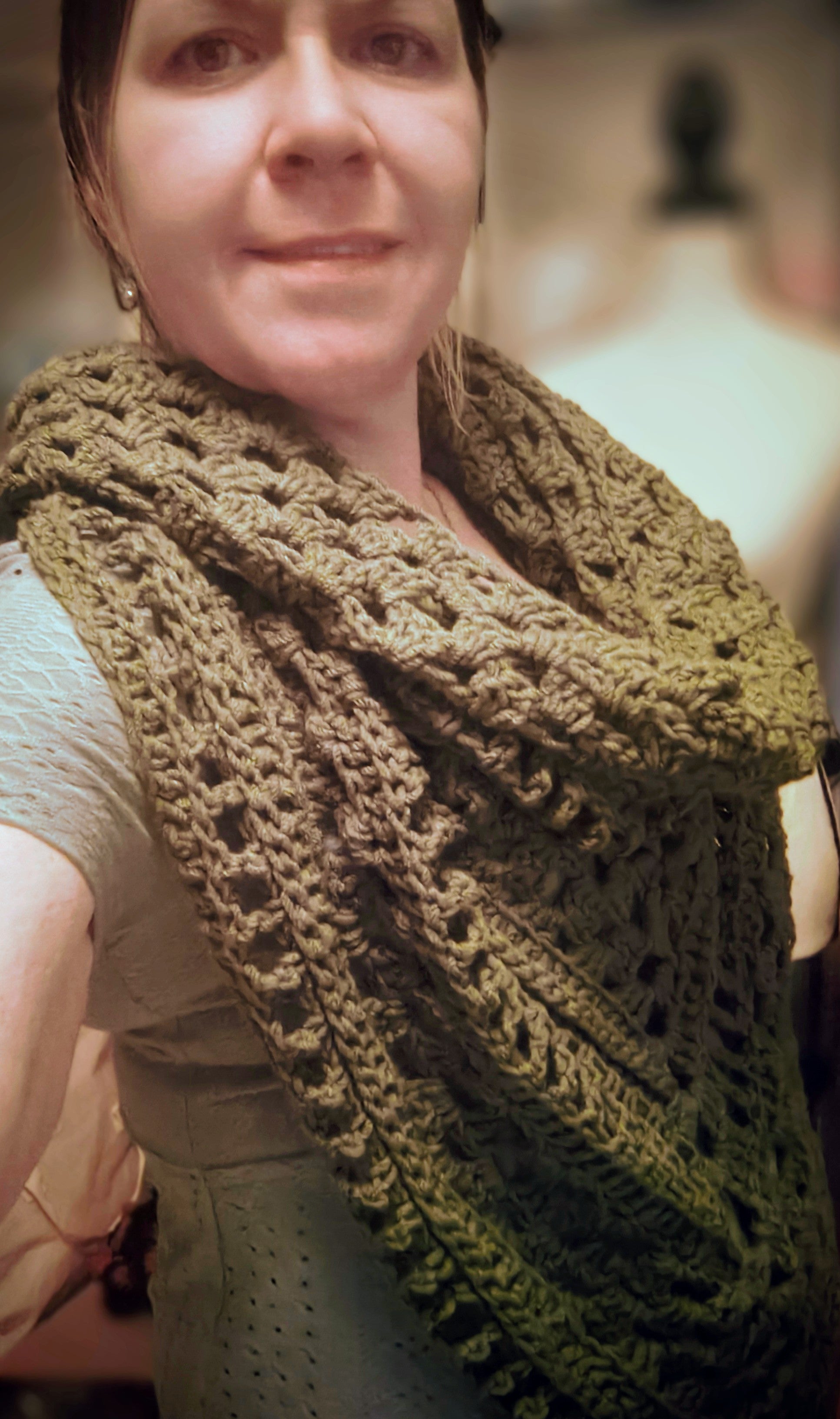Handmade olive green crochet triangle shawl worn by a woman, featuring detailed textured stitching and a soft, cozy drape.